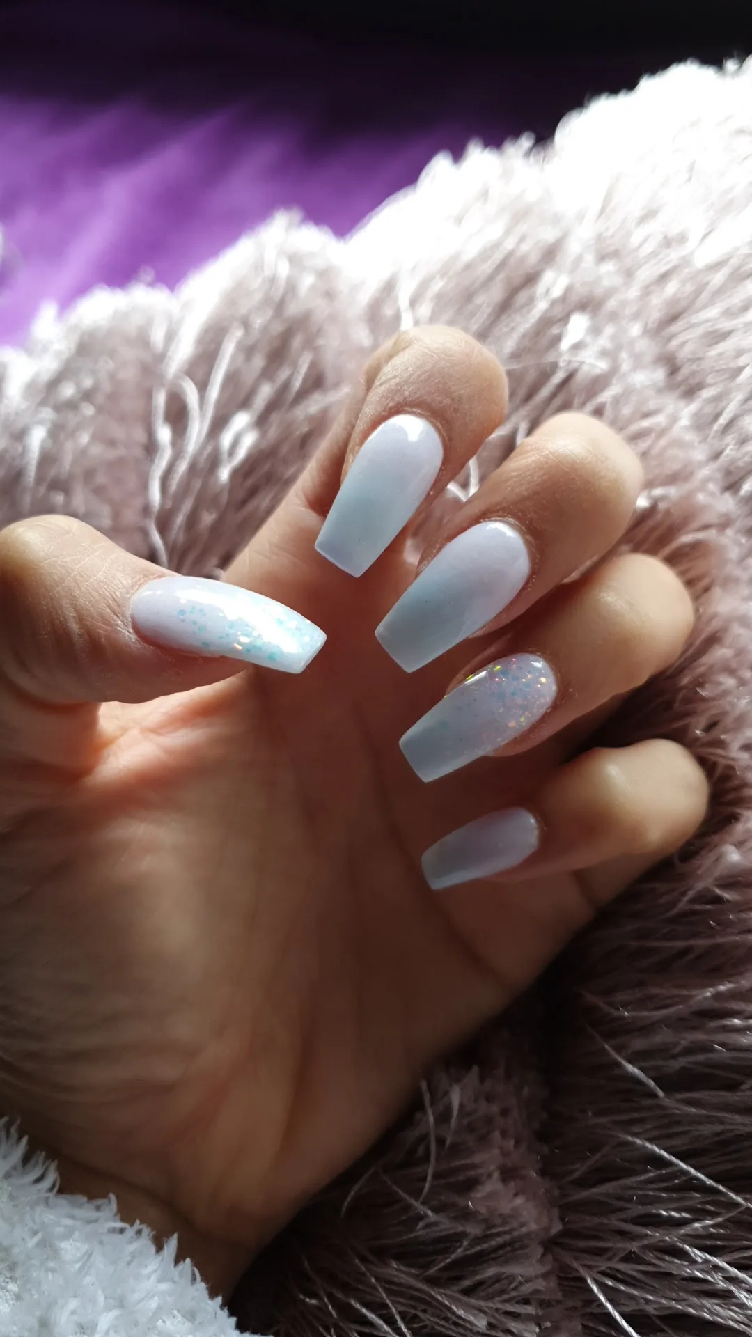 White and pale-blue coffin nails with iridescent glitter on a fluffy blanket with a purple ground