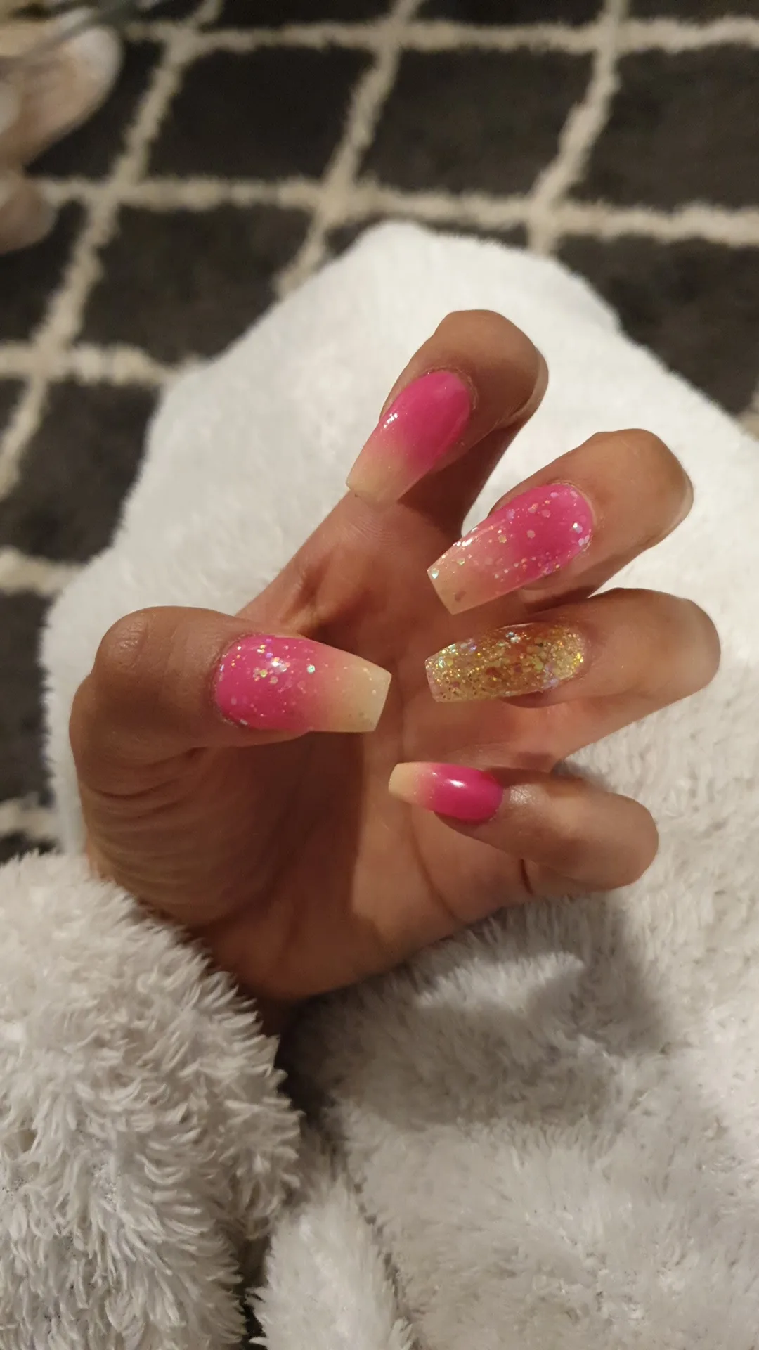 Pink and gold-glitter ombre coffin nails on a white fluffy blanket
