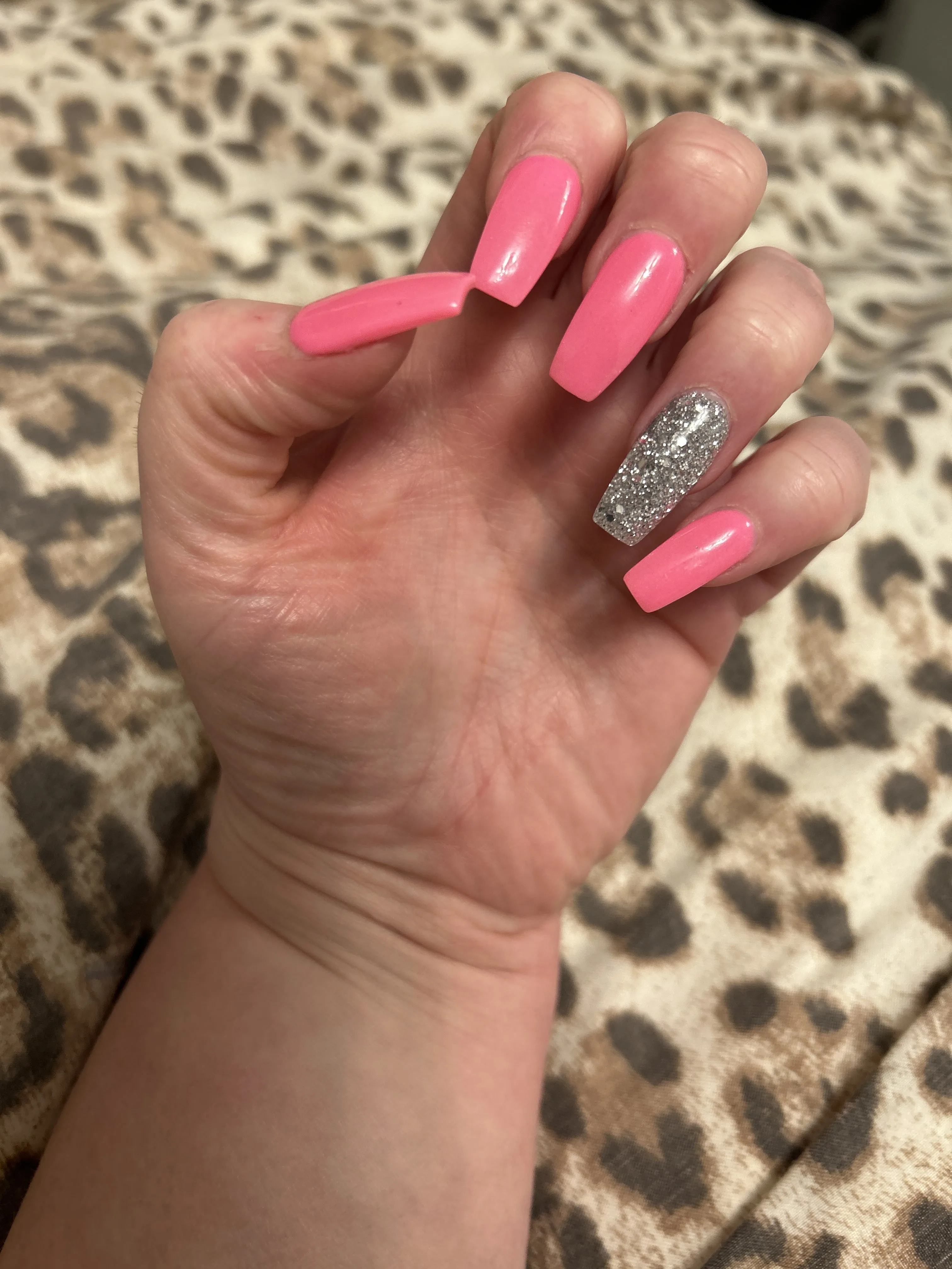 Hot-pink coffin nails with a silver-glitter accent nail on a leopard-print throw