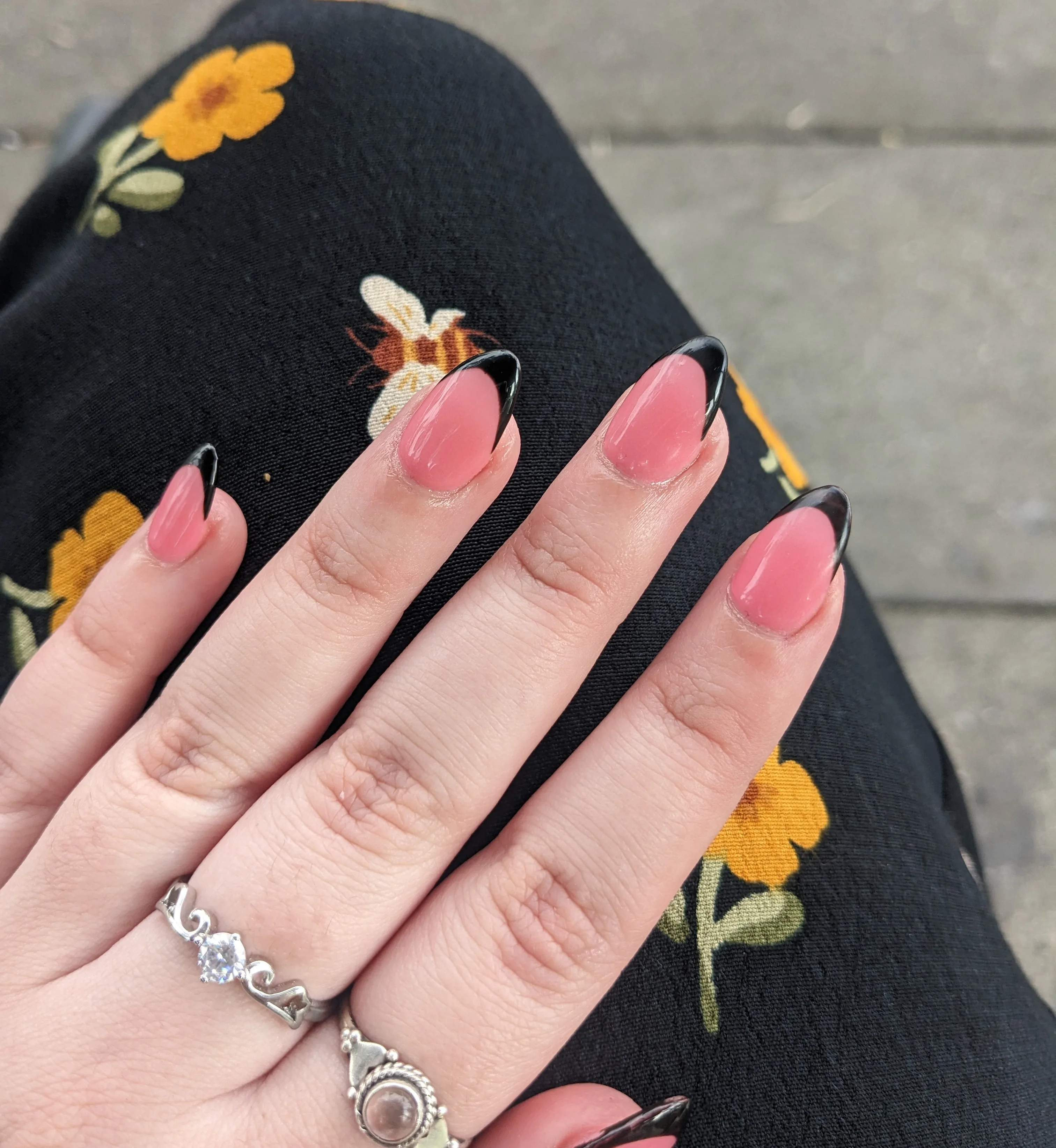 Pink almond nails with black French tips, floral fabric and silver rings