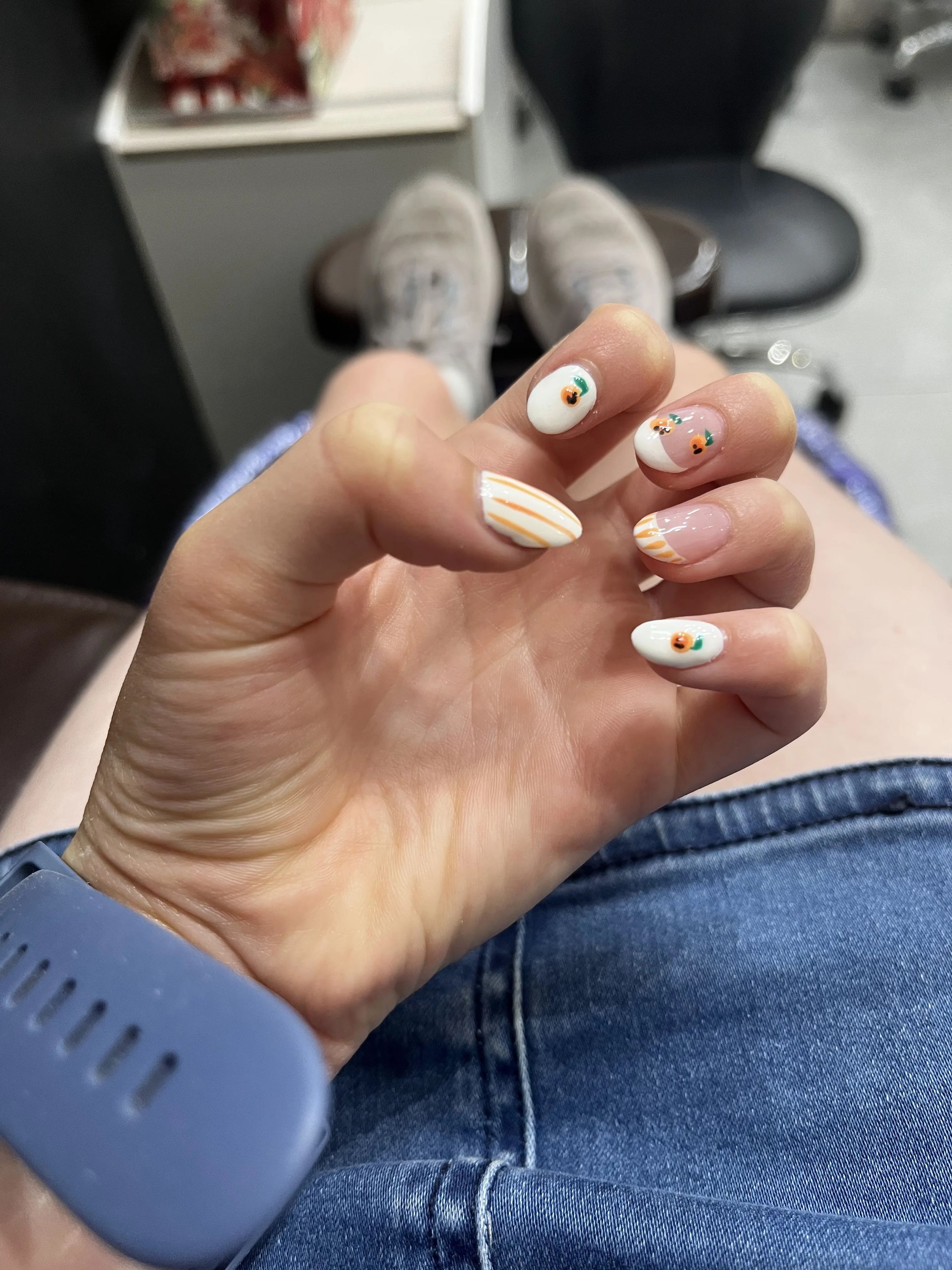 White nails with tiny hand-painted oranges and orange stripe accents, hand over jeans